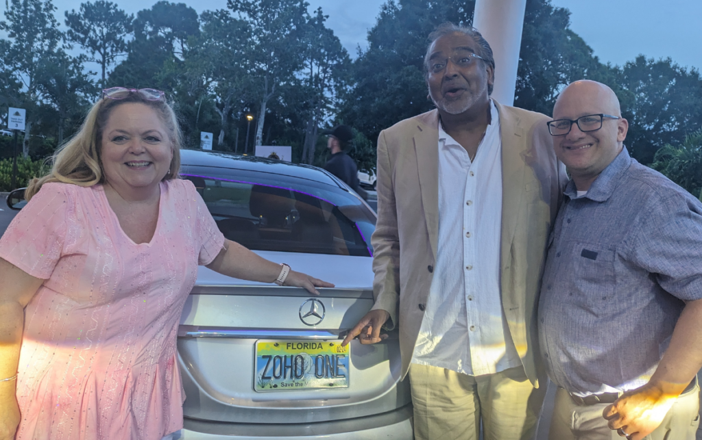 A couple of CRM consultants standing next to a license plate that says: Zoho One.